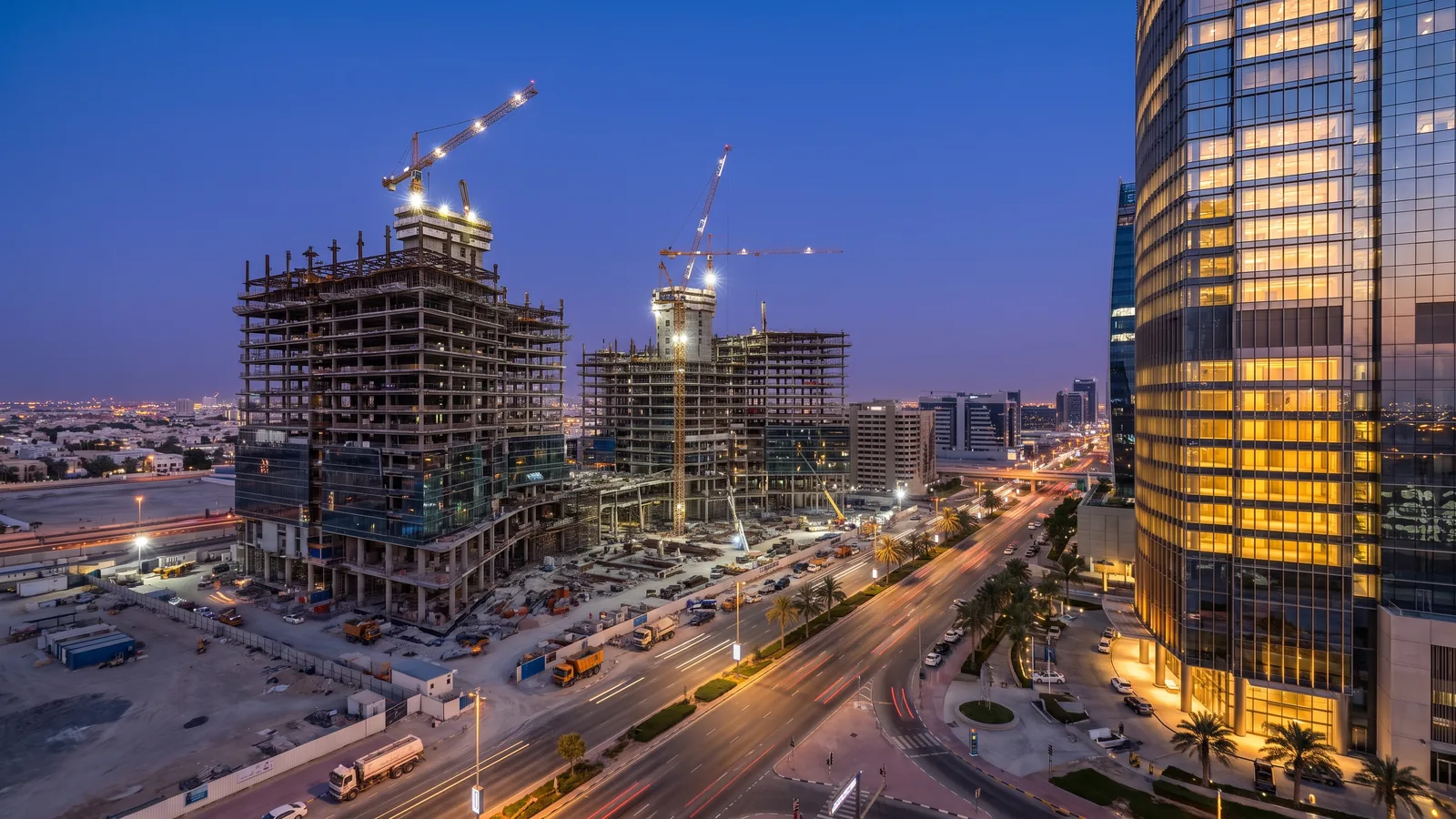 Mixed-use development under construction at dusk beside a completed glass tower